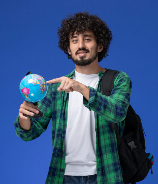 front-view-male-student-green-checkered-shirt-wearing-black-backpack-holding-little-globe-blue-wall
